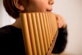 Panflöte aus hellen Rohren in Nahaufnahme, dahinter ein Kind, unscharf