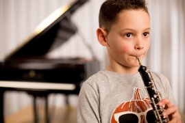 Kind spielt Oboe, im Hintergrund ein Flügel