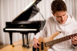 Jugendlicher spielt E-Bass, im Hintergrund ein Flügel