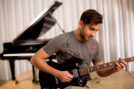 Junger Mann spielt E-Gitarre, im Hintergrund ein Flügel