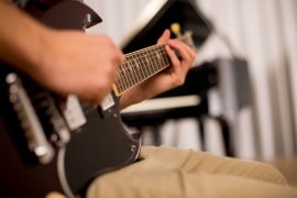 Nahaufnahme von Händen auf Griffbrett und Korpus einer E-Gitarre