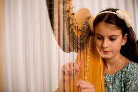 Kind mit Haarband spielt Harfe vor einem hellen Vorhang