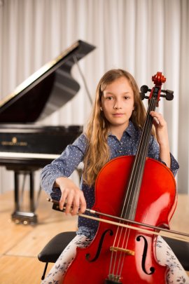 Kind sitzt mit einem Violoncello und Bogen vor einem Flügel