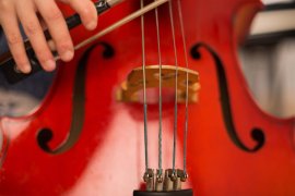 Nahaufnahme eines roten Violoncellos mit Steg, Saiten und Bogen