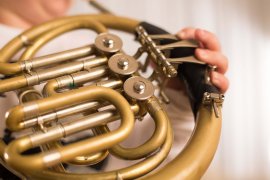 Nahaufnahme eines Waldhorns mit Ventilen und Hebeln, eine Hand hält das Instrument