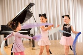 Drei Kinder in Ballettkleidern mit Katzenohren tanzen mit bunten Tüchern vor einem Flügel