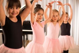 Vier Kinder in Ballettanzügen mit Tutus halten die Arme gerundet über dem Kopf