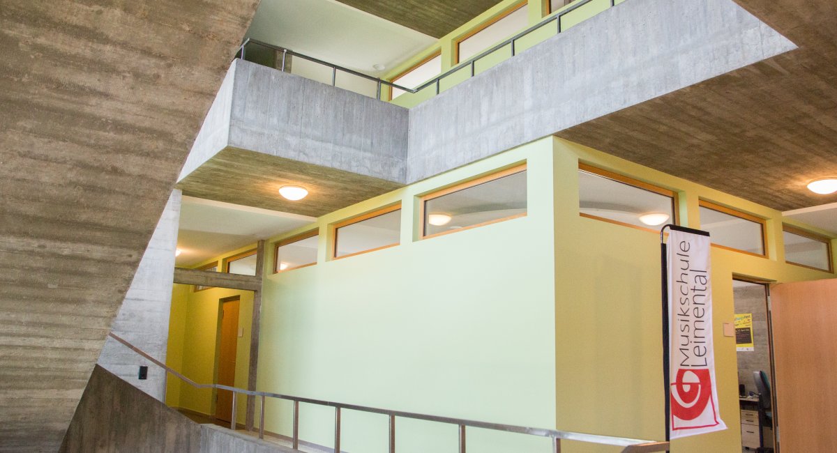 Treppenhaus aus Sichtbeton mit grünen Wänden, daneben eine Fahne «Musikschule Leimental»