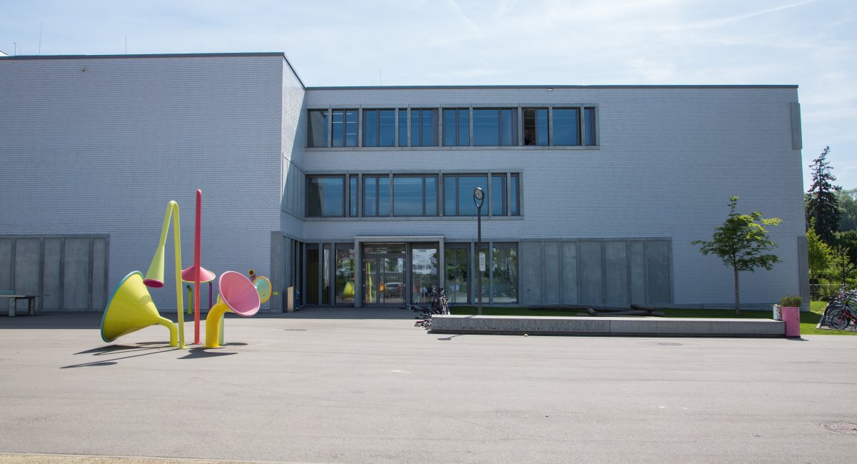 Farbige Trichter-Skulpturen vor einem hellen Schulhaus
