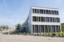 Helles Schulhaus mit Fensterfront, davor aufgereihte Velos am Strassenrand