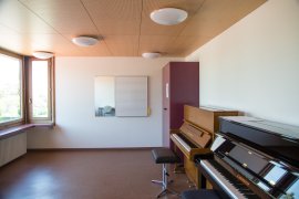 Unterrichtsraum mit zwei Klavieren, Notentafel und Spiegel an der Wand