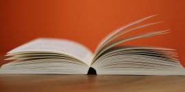 Aufgeschlagenes Buch mit blätternden Seiten vor orangem Hintergrund
